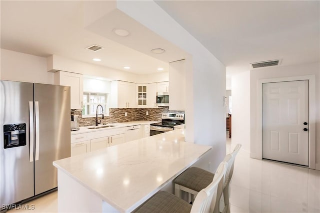 kitchen with white cabinets, stainless steel appliances, a kitchen bar, and sink