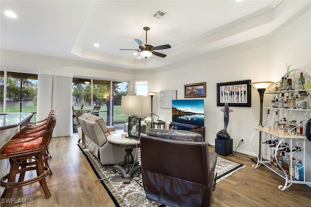 living room with ceiling fan, ornamental molding, a raised ceiling, and hardwood / wood-style floors