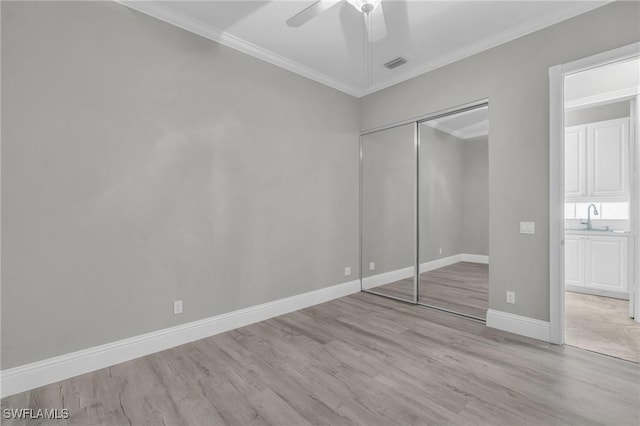 unfurnished bedroom with sink, ceiling fan, crown molding, light wood-type flooring, and a closet