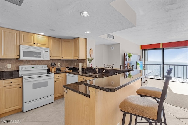 kitchen with light brown cabinetry, a kitchen breakfast bar, white appliances, and kitchen peninsula