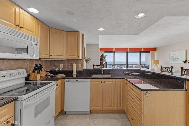 kitchen with sink, white appliances, a textured ceiling, and dark stone counters