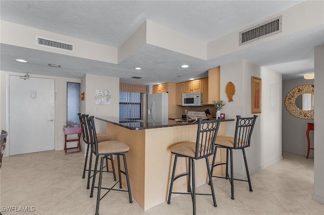 kitchen featuring stainless steel refrigerator with ice dispenser, a kitchen bar, dark stone counters, kitchen peninsula, and stove