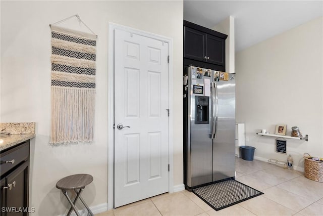 kitchen with stainless steel refrigerator with ice dispenser, light tile patterned flooring, and light stone counters