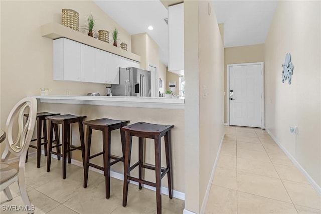 kitchen featuring a kitchen breakfast bar, light tile patterned flooring, white cabinetry, and high end fridge