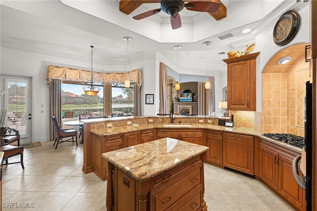 kitchen featuring a kitchen island, decorative light fixtures, stainless steel gas stovetop, sink, and light stone countertops