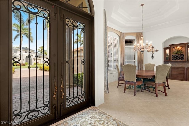 tiled entryway with a wealth of natural light, ornamental molding, a tray ceiling, an inviting chandelier, and french doors