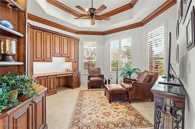 sitting room featuring light tile patterned flooring, built in desk, ornamental molding, a raised ceiling, and ceiling fan