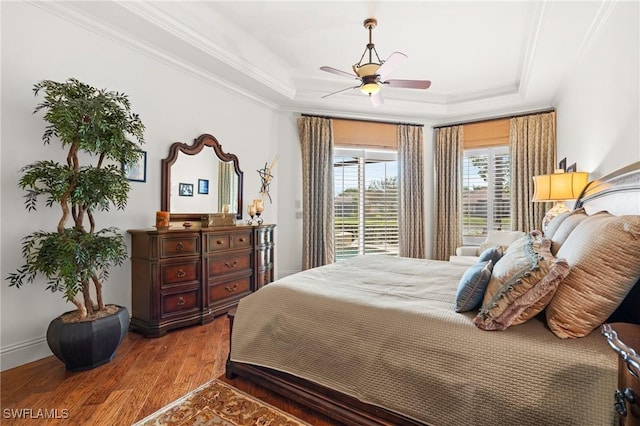 bedroom featuring hardwood / wood-style flooring, ceiling fan, ornamental molding, and a tray ceiling