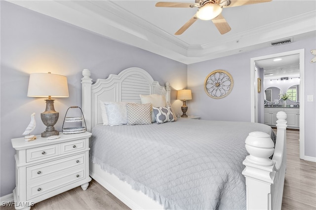 bedroom featuring ensuite bath, ornamental molding, light hardwood / wood-style flooring, ceiling fan, and a tray ceiling