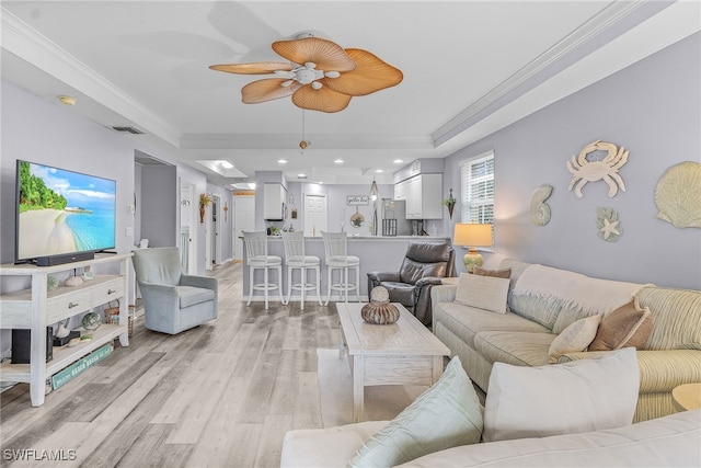 living room featuring a tray ceiling, crown molding, visible vents, light wood-style flooring, and a ceiling fan