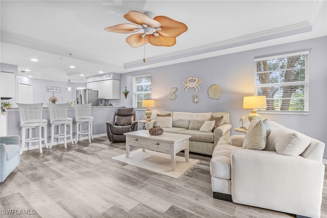 living room featuring ceiling fan, a tray ceiling, light hardwood / wood-style flooring, and ornamental molding