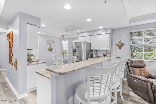 kitchen with kitchen peninsula, stainless steel fridge with ice dispenser, hanging light fixtures, and a raised ceiling