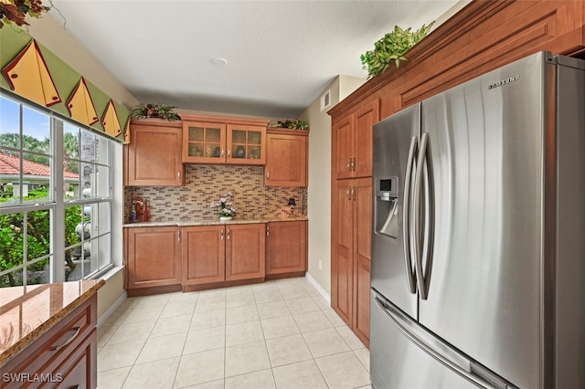 kitchen with a wealth of natural light, stainless steel fridge, light stone counters, and decorative backsplash