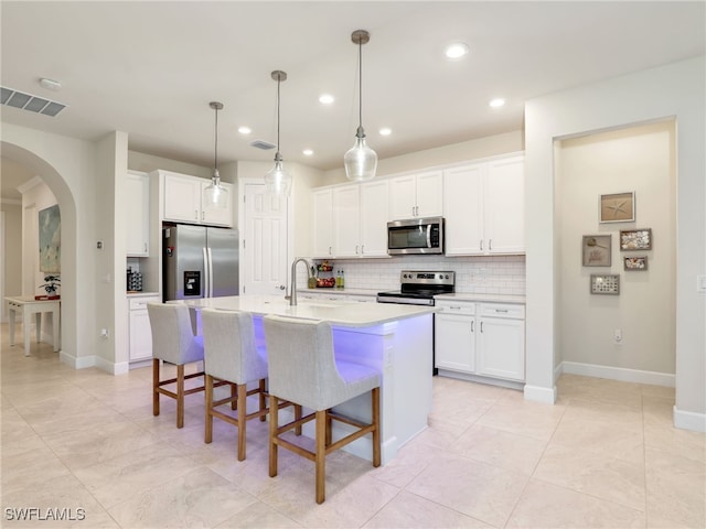 kitchen with stainless steel appliances, white cabinetry, a center island with sink, and decorative backsplash