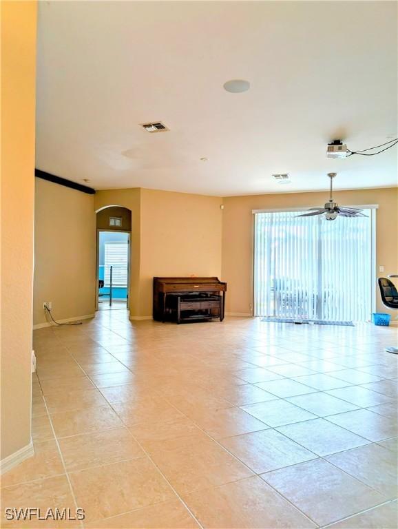 unfurnished room featuring arched walkways, light tile patterned floors, visible vents, baseboards, and a ceiling fan