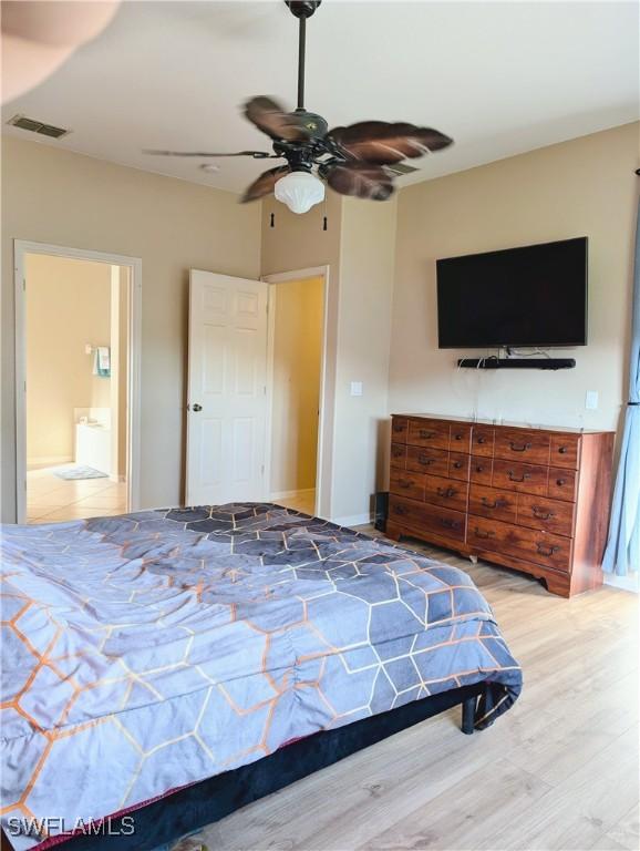 bedroom with a ceiling fan, connected bathroom, visible vents, and wood finished floors