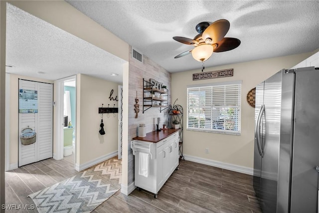 kitchen with stainless steel refrigerator, white cabinetry, butcher block counters, and a textured ceiling