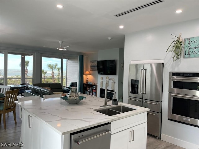 kitchen featuring sink, appliances with stainless steel finishes, a kitchen island with sink, light stone counters, and white cabinets