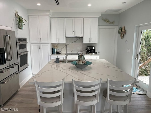 kitchen with tasteful backsplash, white cabinets, light stone countertops, dark wood-type flooring, and a center island with sink