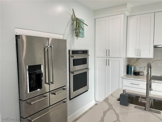 kitchen featuring light stone counters, sink, stainless steel appliances, and white cabinets