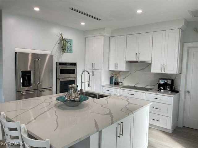 kitchen featuring a kitchen island with sink, light stone counters, and appliances with stainless steel finishes