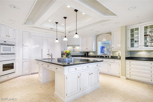 kitchen featuring white cabinetry, crown molding, decorative light fixtures, a center island with sink, and white appliances