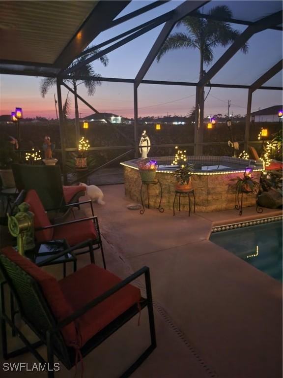 patio terrace at dusk with a swimming pool with hot tub, exterior bar, and glass enclosure