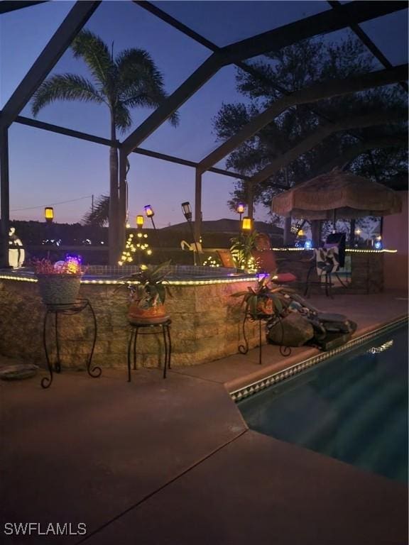 pool at dusk with a patio and a lanai