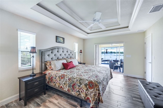 bedroom with a tray ceiling, baseboards, visible vents, and wood finished floors