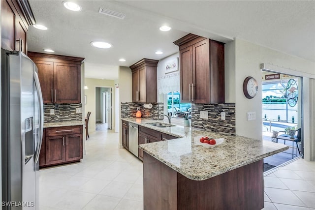 kitchen with light stone counters, visible vents, a peninsula, a sink, and stainless steel appliances