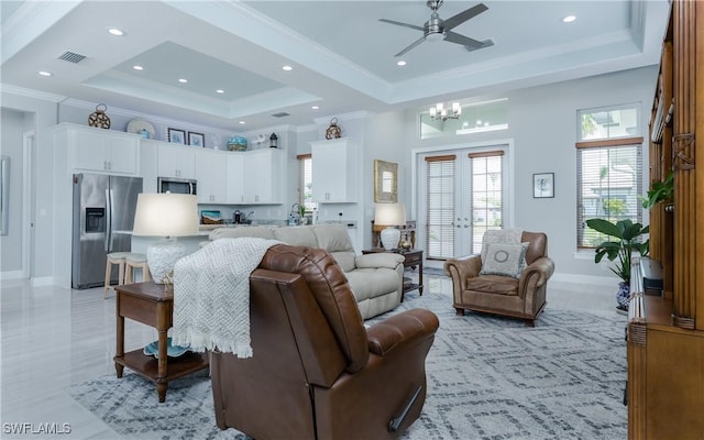 living room featuring ceiling fan with notable chandelier, a high ceiling, light tile patterned floors, a tray ceiling, and crown molding