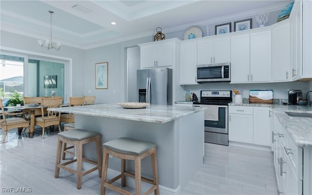 kitchen featuring hanging light fixtures, a kitchen island, stainless steel appliances, light stone countertops, and white cabinets