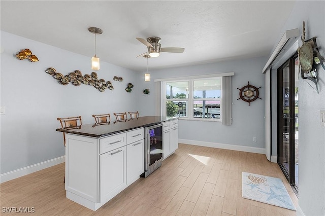 kitchen featuring white cabinetry, hanging light fixtures, light wood-type flooring, ceiling fan, and wine cooler