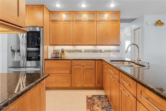 kitchen featuring stainless steel refrigerator with ice dispenser, sink, decorative backsplash, and dark stone counters