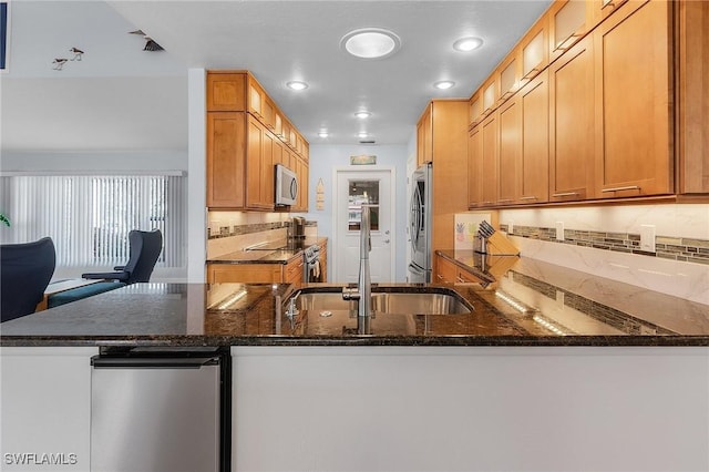 kitchen with tasteful backsplash, dark stone counters, sink, kitchen peninsula, and stainless steel appliances