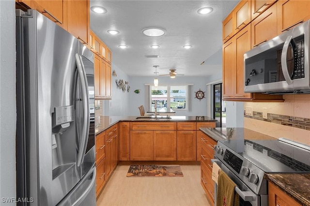 kitchen with kitchen peninsula, pendant lighting, appliances with stainless steel finishes, sink, and dark stone counters