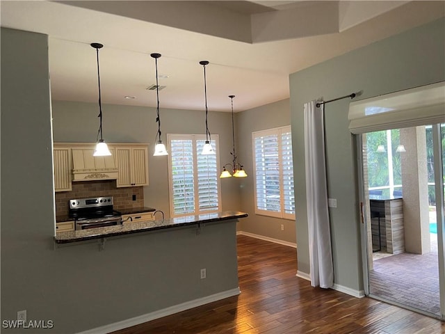 kitchen with dark wood-type flooring, dark stone countertops, cream cabinets, stainless steel electric range oven, and kitchen peninsula