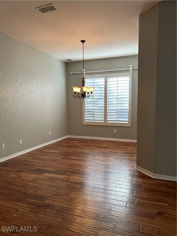 spare room with dark hardwood / wood-style flooring and an inviting chandelier