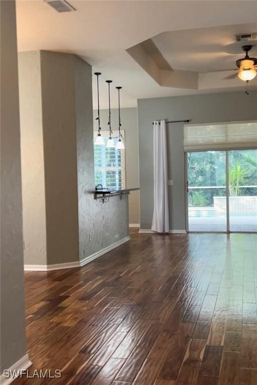 unfurnished dining area with dark wood-type flooring, a wealth of natural light, ceiling fan, and a tray ceiling