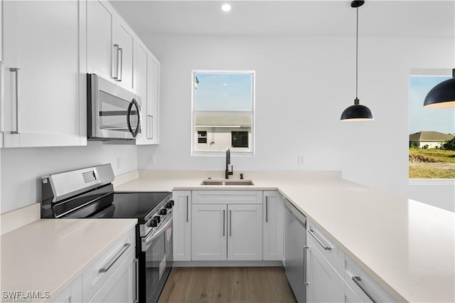 kitchen with sink, stainless steel appliances, white cabinetry, and decorative light fixtures