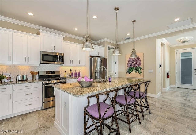 kitchen with decorative light fixtures, white cabinets, stainless steel appliances, and an island with sink