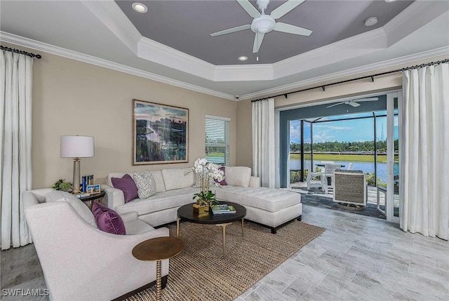 living room featuring ceiling fan, crown molding, a raised ceiling, and a water view