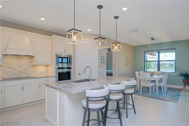6217 Harmony Dr, Ave Maria, FL 34142 - kitchen with tasteful backsplash, a sink, appliances with stainless steel finishes, premium range hood, and light stone counters