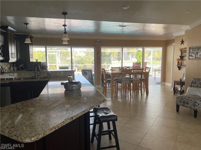 kitchen with light tile patterned floors, stone countertops, ornamental molding, dark cabinets, and decorative light fixtures