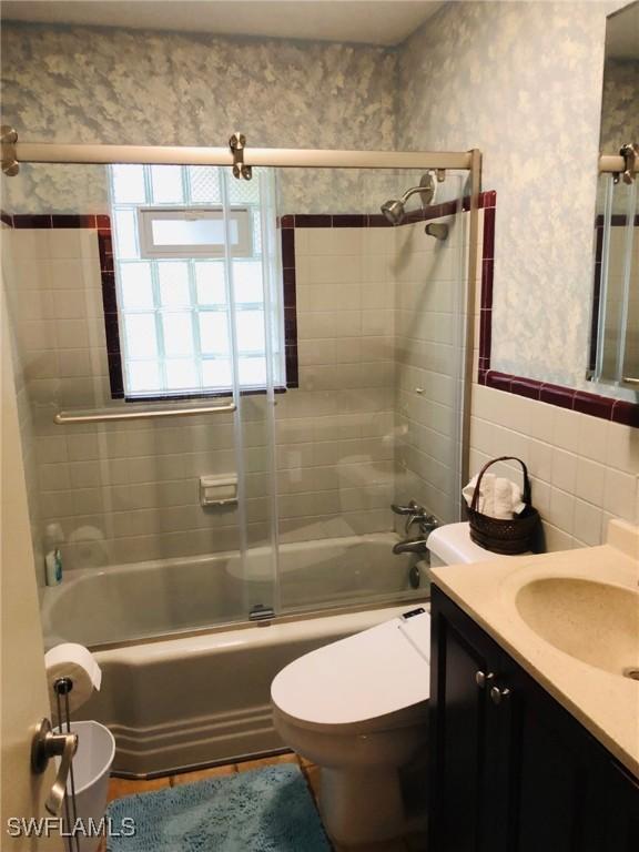 full bathroom with vanity, combined bath / shower with glass door, tile walls, and toilet