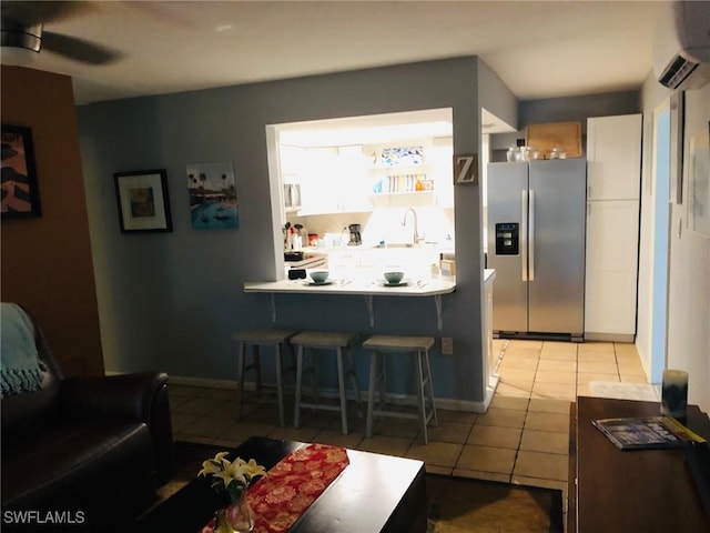 kitchen featuring light tile patterned floors, stainless steel fridge, white cabinetry, a kitchen breakfast bar, and an AC wall unit