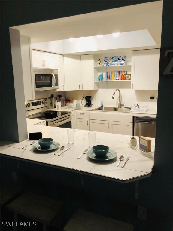 kitchen featuring light stone counters, stainless steel appliances, sink, and white cabinets