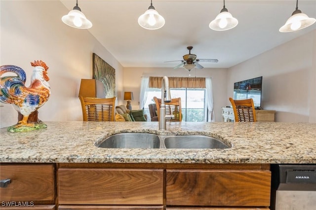 kitchen featuring light stone counters, pendant lighting, a ceiling fan, and a sink