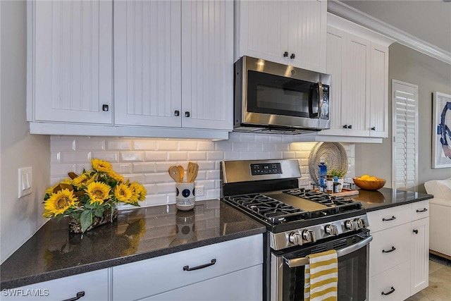 kitchen with crown molding, appliances with stainless steel finishes, tasteful backsplash, white cabinetry, and dark stone countertops