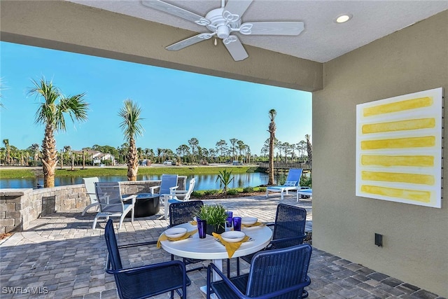 view of patio with an outdoor fire pit, a water view, and ceiling fan